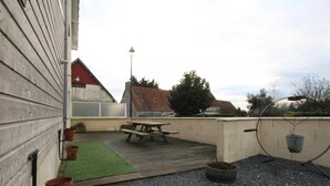 A patio area with a picnic table, potted plants, and a small garden. - Charming house with enclosed garden in Cotentin Marshes (Liesville-sur-Douve)