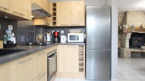 A modern kitchen with wooden cabinets, stainless steel appliances, and a stone fireplace. - Charming house with enclosed garden in Cotentin Marshes (Liesville-sur-Douve)