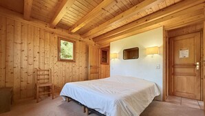 Un dormitorio de cabaña de madera con una cama, una silla, una ventana y una puerta.