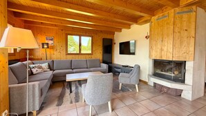 Una sala de estar acogedora con techo de madera, chimenea, sofá, mesa de centro y televisor.