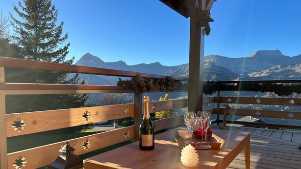 Una terraza de madera con una mesa para dos, una botella de vino y un piñón decorativo.