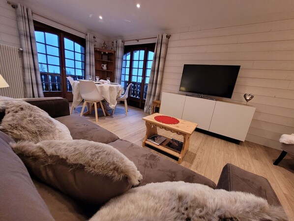 A modern living room with a sofa, a small wooden table, and a TV on a white cabinet.