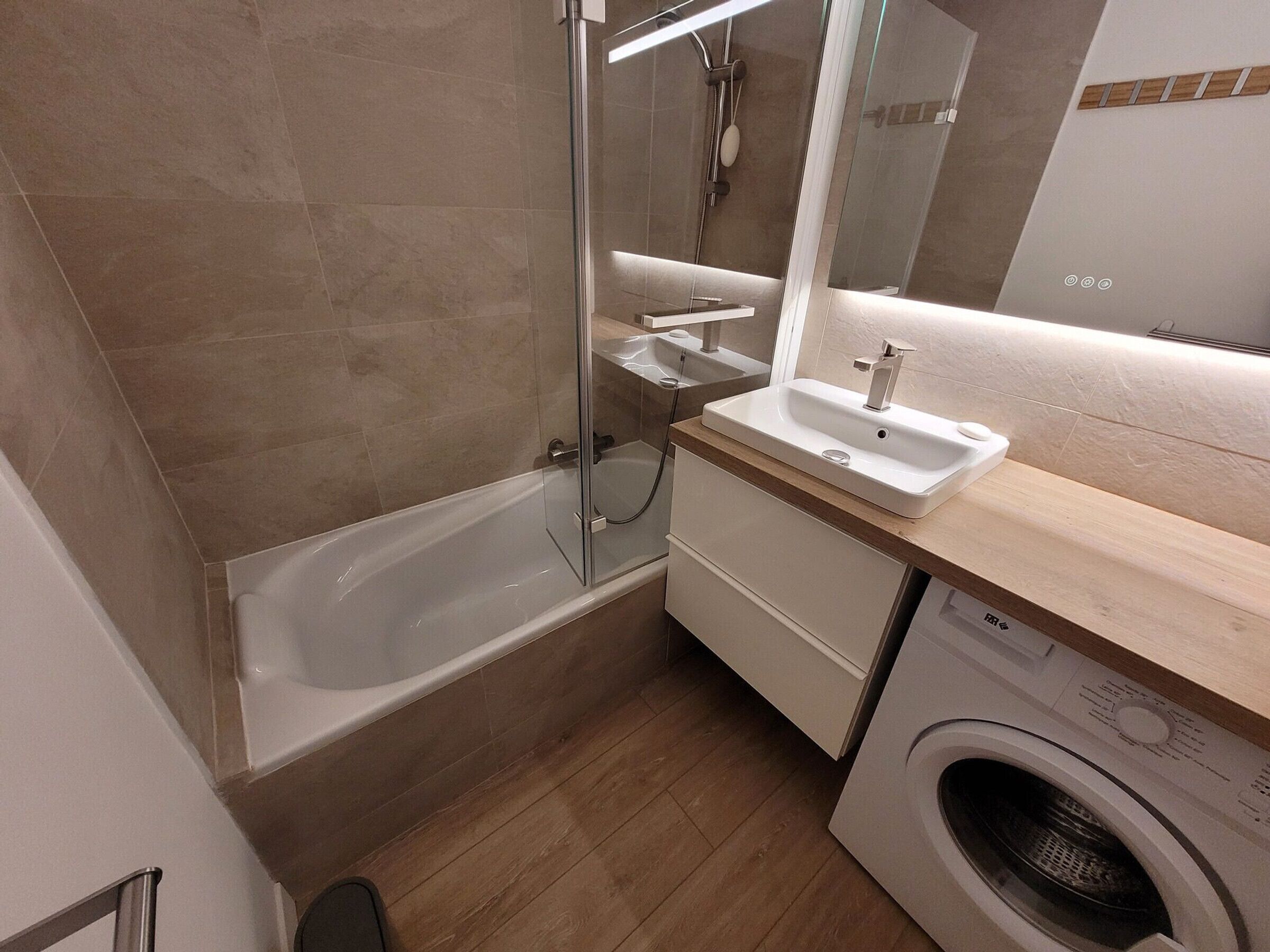 Een moderne badkamer met een badkuip, een wastafel, een spiegel en een wasmachine.