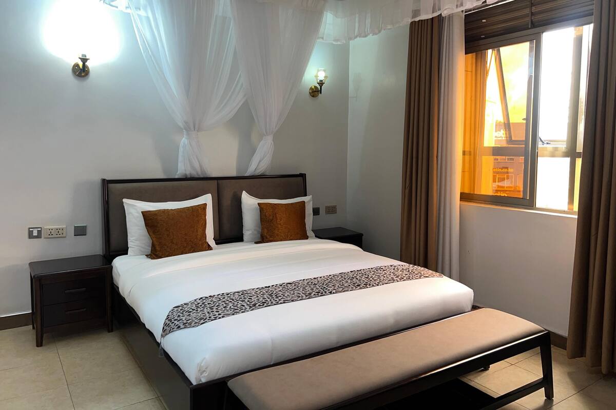 Quarto de hotel bem organizado, com uma cama grande, mesas de cabeceira e uma janela com cortinas.