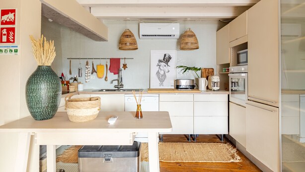 Cocina moderna con armarios blancos, encimera de madera y una cesta colgante.