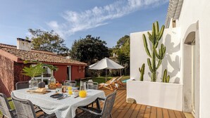 Una terraza de madera con una mesa lista para el desayuno, sillas exteriores y una maceta con cactus.