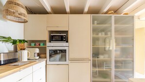 Una cocina moderna con armarios blancos, microondas, horno y despensa con puerta de vidrio.