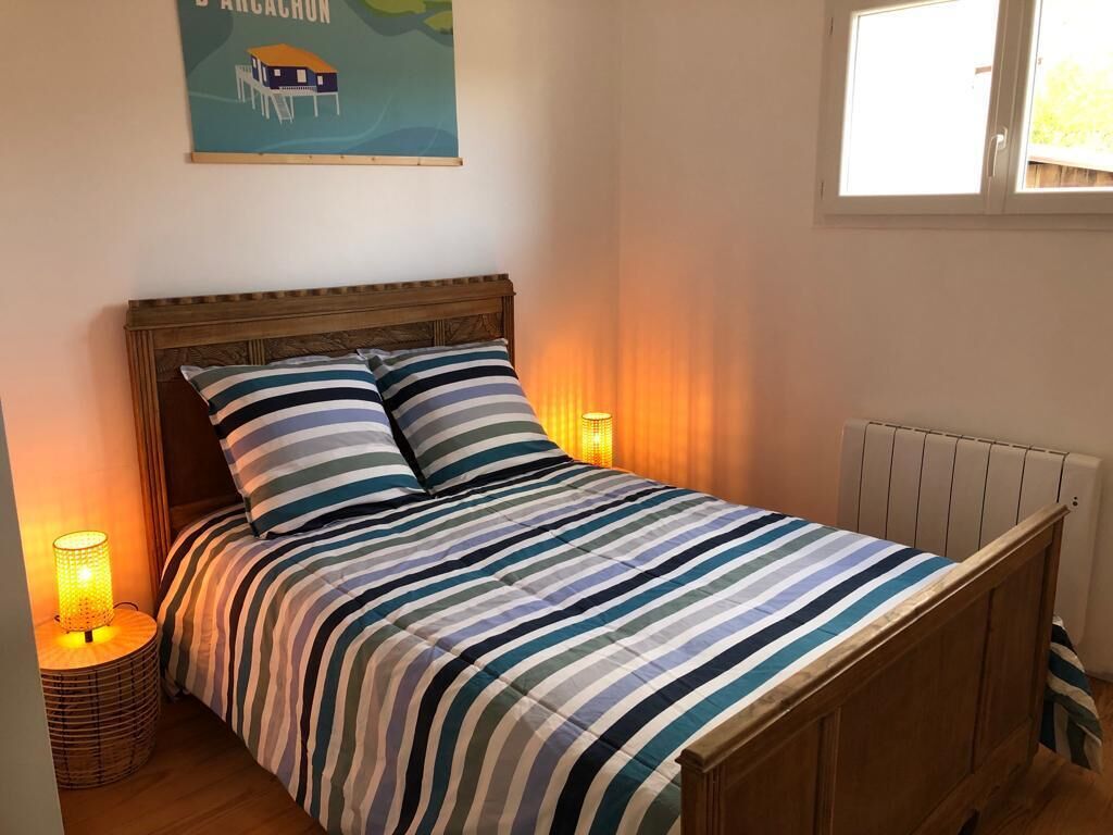A bed with a striped bedspread and two pillows, a wooden headboard, a nightstand with a lamp, and a poster on the wall.