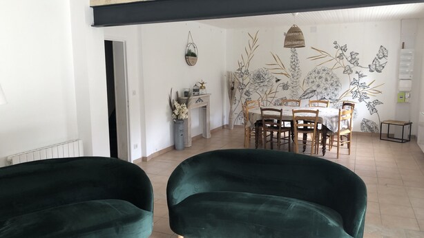 A modern living room with two green velvet armchairs, a wooden coffee table, a dining area with a white table and wooden chairs, and a wall with a floral mural. - THE SIGNORET HOUSE IN THE COUNTRYSIDE NEAR BORDEAUX (Baron)