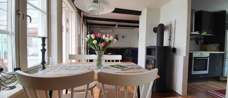 A dining area with a table set for two, a vase of tulips, and a hanging light fixture.