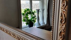 Un espejo con un marco decorativo refleja una ventana, una planta en maceta y un balaustrada blanca.