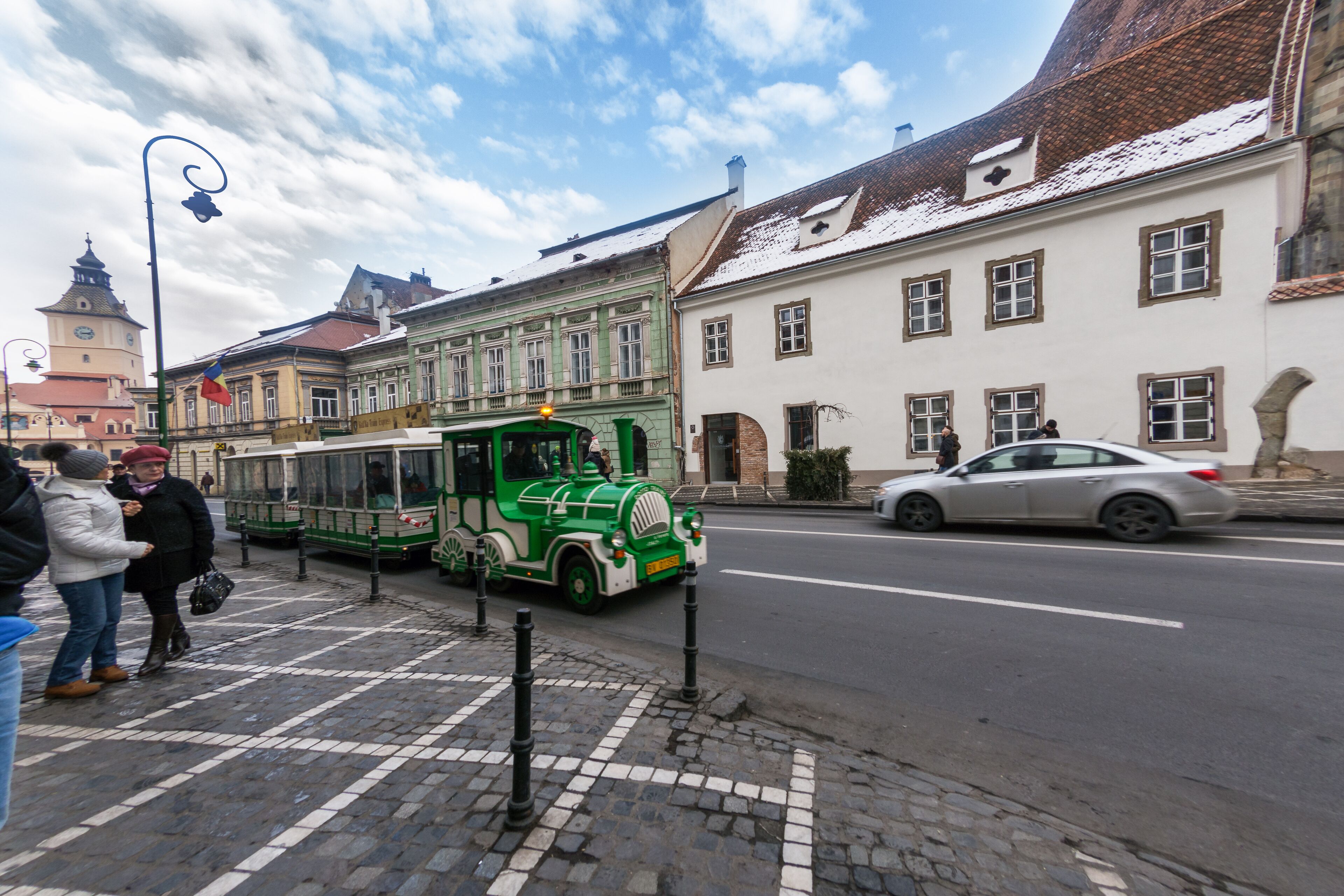 A street scene with a green tram, cobblestone pavement, and historic buildings.
