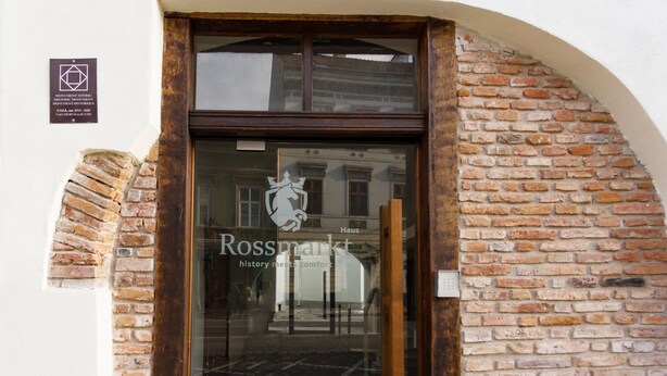 A hotel entrance with a glass door, a sign reading "Rossmarket," and a plaque above the door. -  Rossmarkt Haus (Brasov)