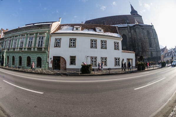A street view with a white building with multiple windows and a green building with arched windows.
