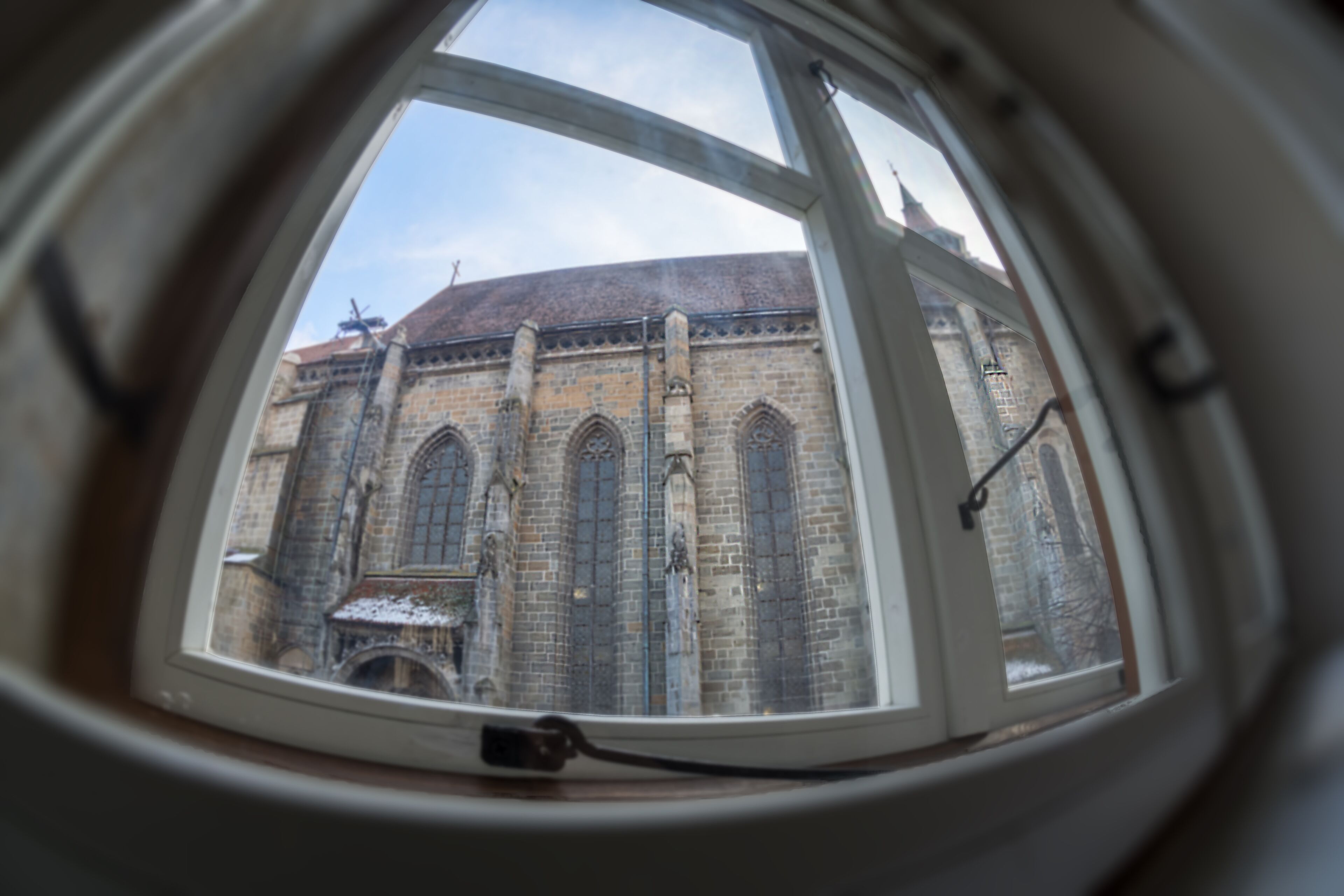 Une vue à travers une fenêtre d’un bâtiment à la façade en briques et aux fenêtres en arc de cercle.