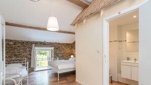 Une chambre avec un mur en pierre, un lit, une lampe suspendue et une vue sur l’extérieur.