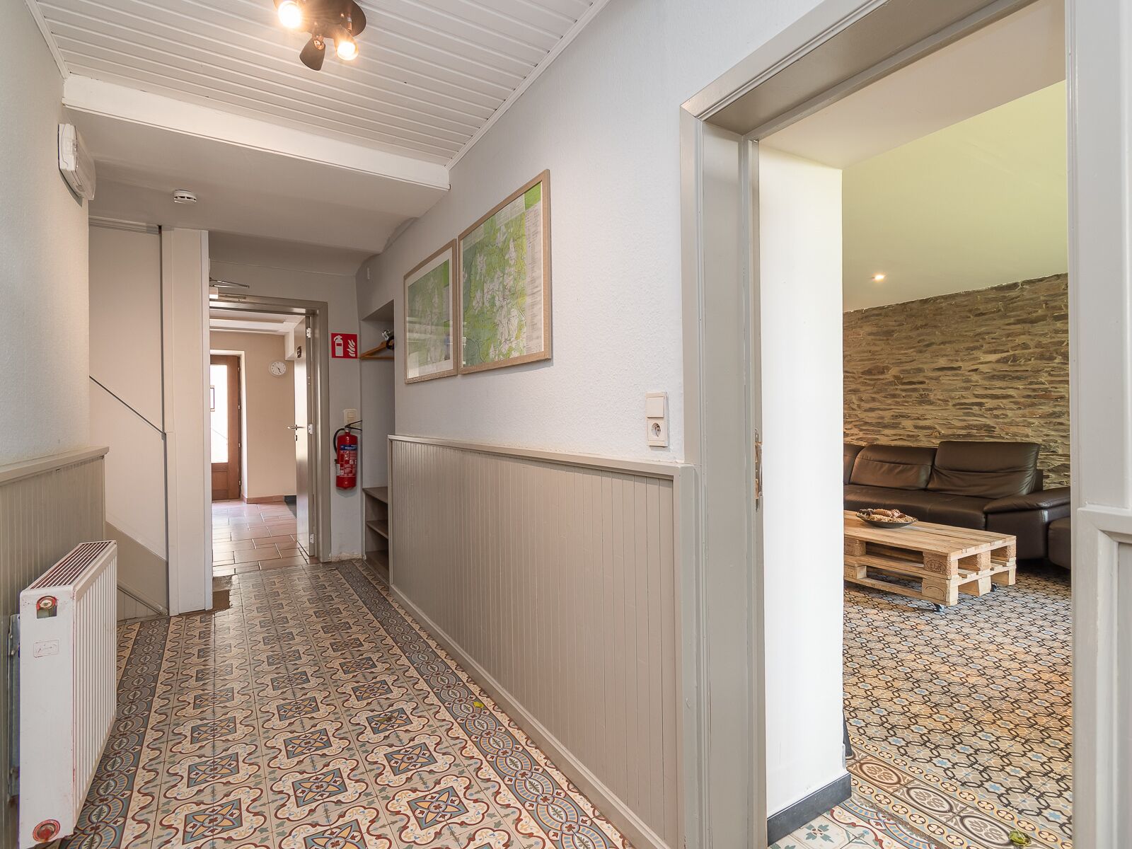 A hallway with patterned floor tiles, a radiator, a fire extinguisher, and a wooden bench.