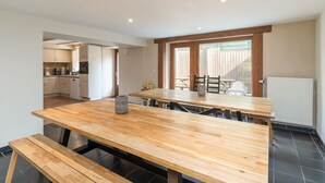 Une cuisine moderne avec des meubles blancs, une table à manger en bois et une vue sur l’extérieur.