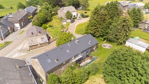 Une zone rurale avec une grande maison dotée d’un toit en pente, d’une allée et d’un paysage environnant composé d’arbres et de champs ouverts.