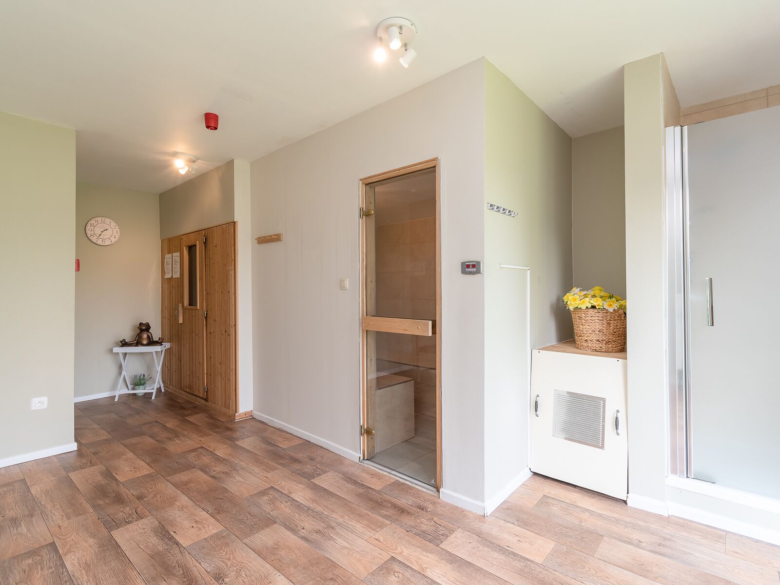 A hallway with wooden flooring, a clock, a wooden door, a glass door, and a refrigerator with flowers.