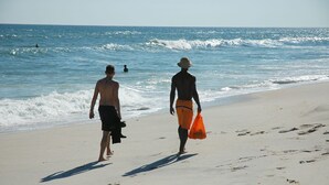 Two people walking on a sandy beach with waves in the background.