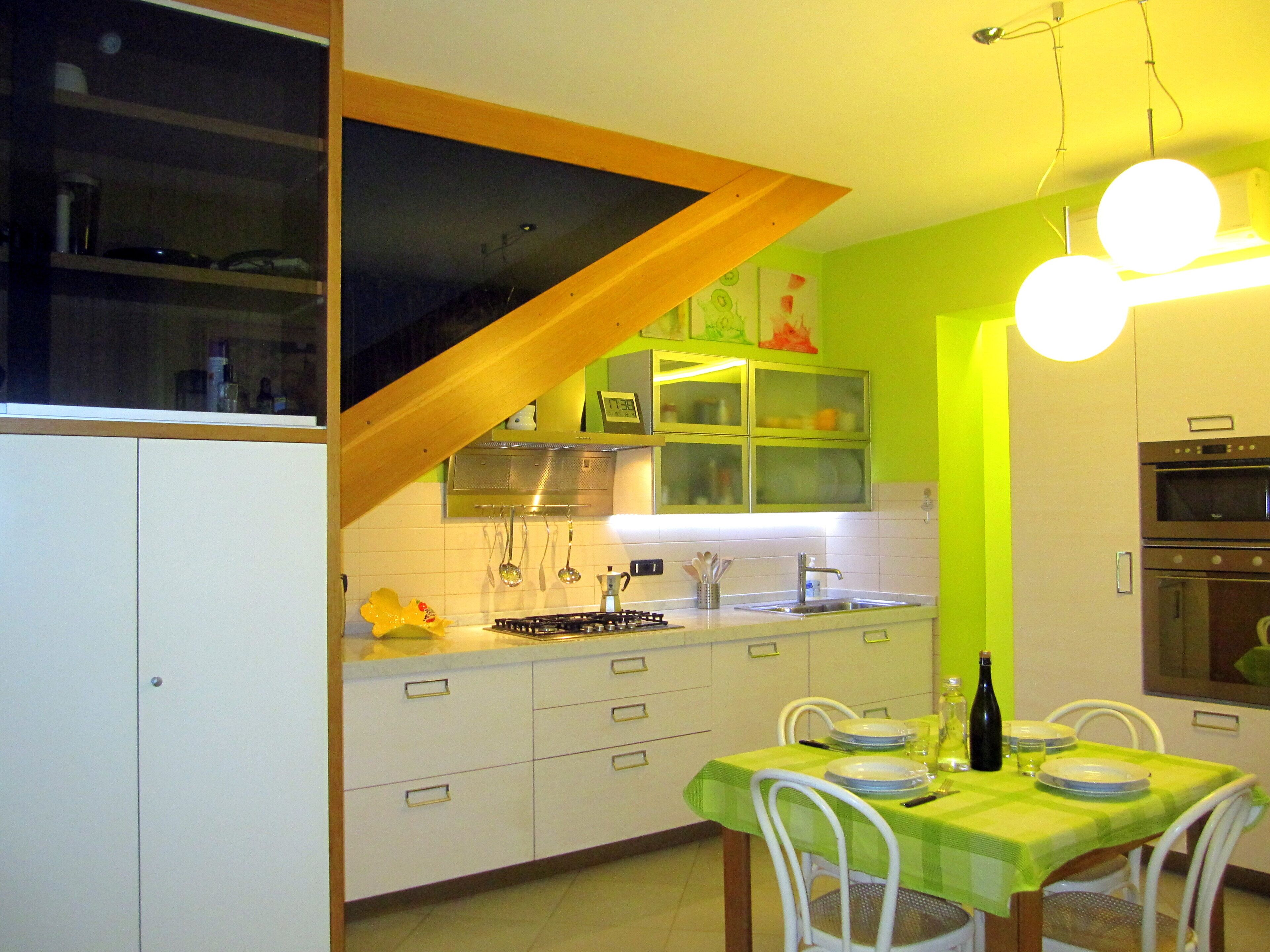 Une cuisine avec des meubles blancs, un mur vert et un coin repas avec une table mise pour deux personnes.