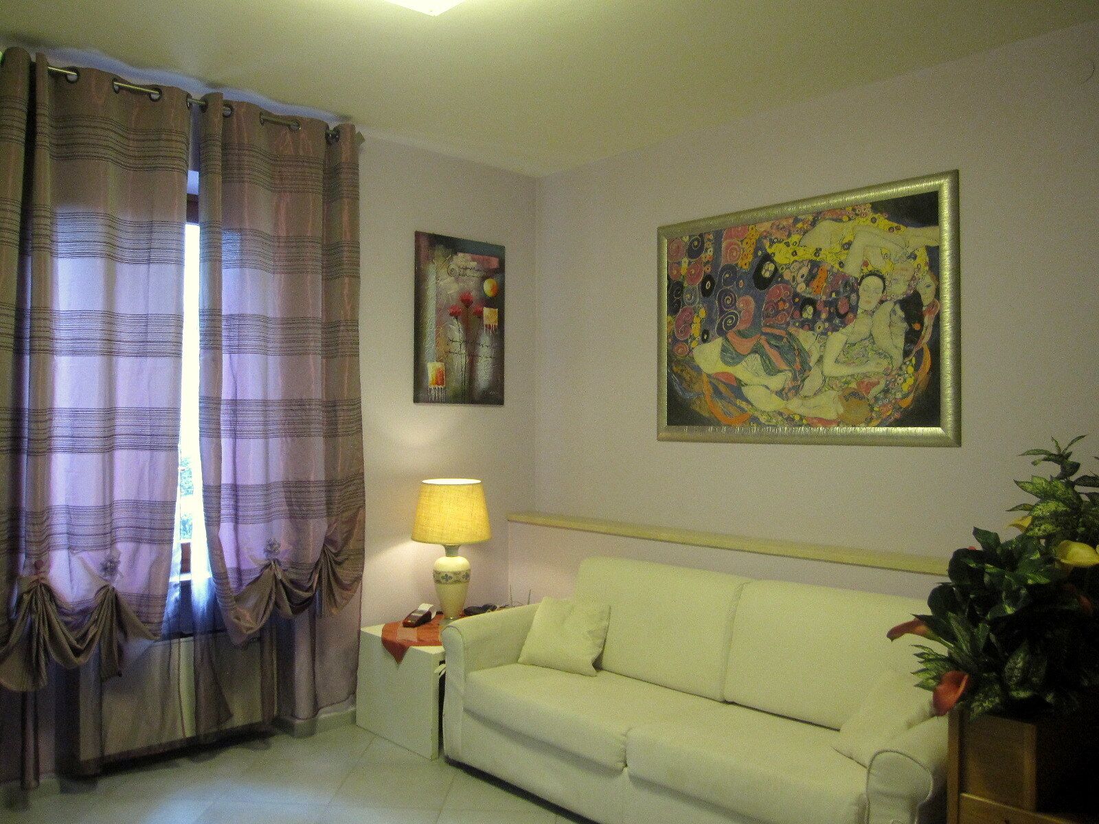A living room with a sofa, a lamp, a painting, and curtains.