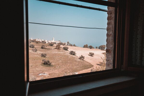 Une vue depuis une fenêtre donnant sur un paysage rural, avec des bâtiments et des arbres.
