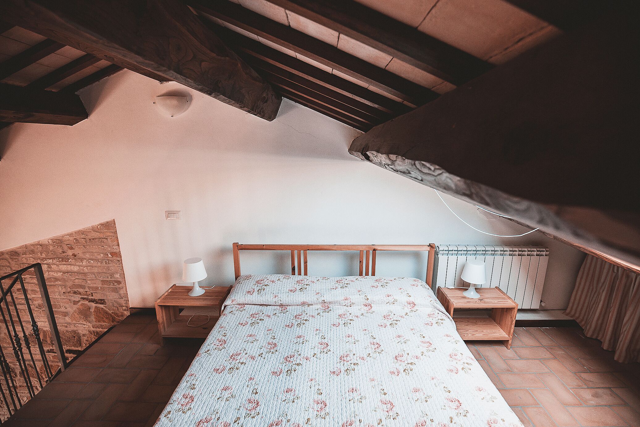 Une chambre à coucher avec une tête de lit en bois, deux tables de chevet avec des lampes, un radiateur et un plafond en pente.