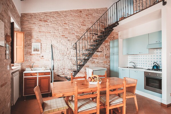 A kitchen with a brick wall, a wooden dining table with chairs, a staircase, and a sink. - Apartment with a pool in the Tour des Palmiers with ocean views—5 minutes from the beach (Marche)