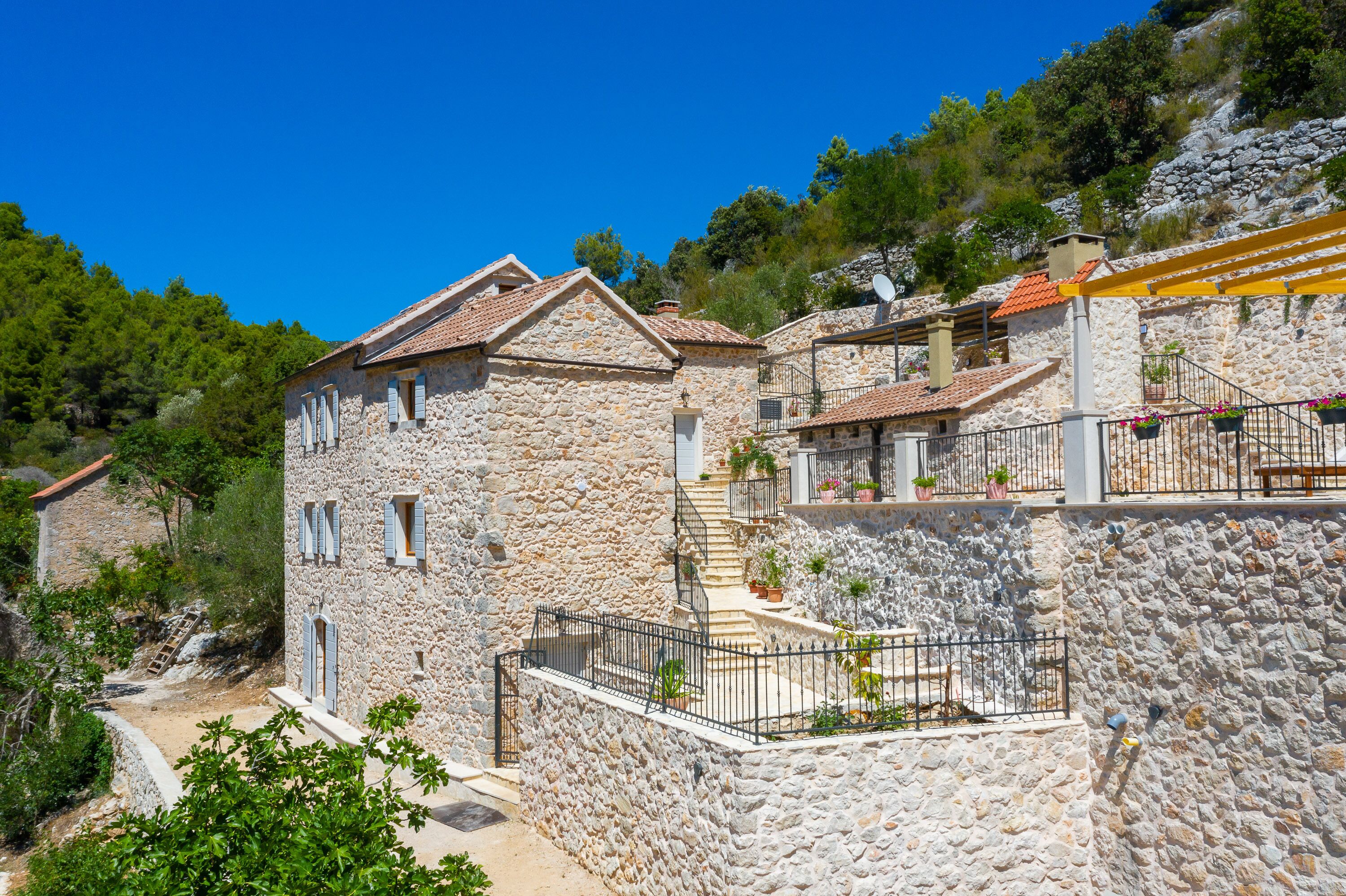 A stone building with a staircase, a balcony with potted plants, and a view of the surrounding landscape.