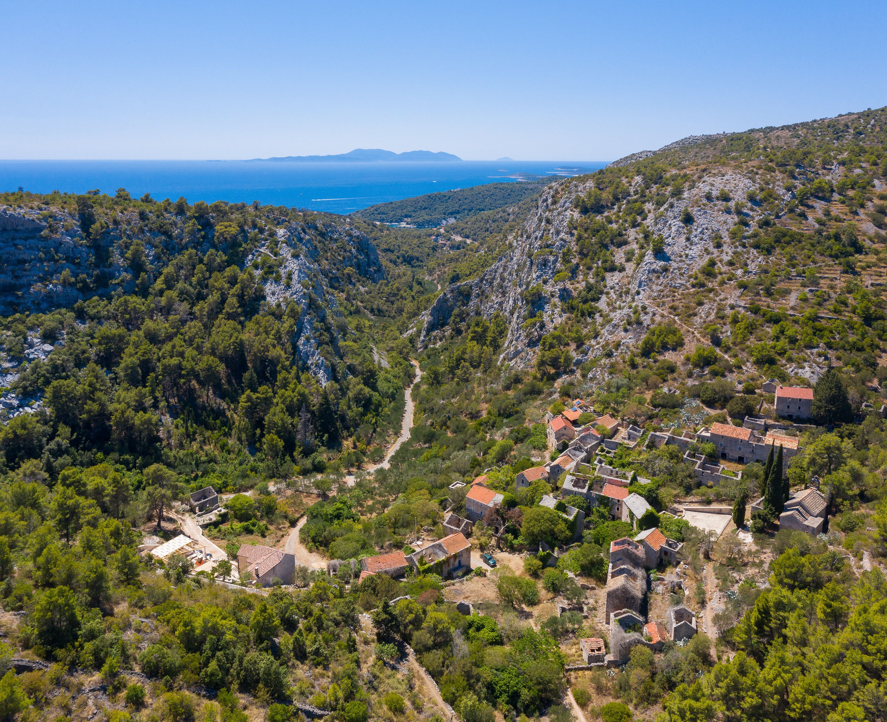 A mountainous village with traditional stone buildings and a clear view of the sea.