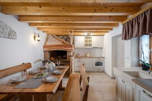 A wooden dining table set with plates, glasses, and a bench. A kitchen with white cabinets and a stove is visible in the background. - Rustic luxury villa Fulmin (Hvar)