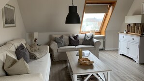 Un loft acollidor amb un sostre alt, un sofà blanc amb coixins, una taula de centre de fusta i un armari blanc.