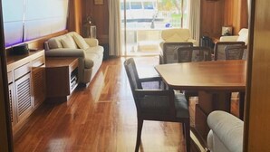 Amplia habitación con piso de madera, un sofá, una mesa de comedor con sillas y un ventanal que ofrece vistas al exterior.