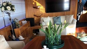 Una mesa de comedor dispuesta con platos, una tetera y cristalería, rodeada por un sofá y objetos decorativos.