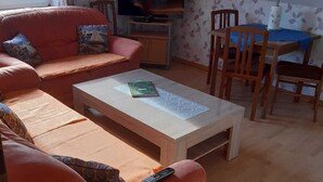 Een woonkamer met een bank, salontafel, televisie en een eethoek met stoelen en een tafel.