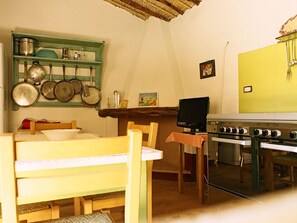 Eine Küche mit Herd, Backofen und hängenden Töpfen. Es gibt einen Tisch mit Stühlen und einen Fernseher auf einem Schrank.
