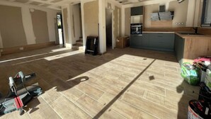 Une pièce spacieuse dotée d’un plancher en bois, d’un coin cuisine avec des meubles gris et d’une grande fenêtre laissant entrer la lumière naturelle.