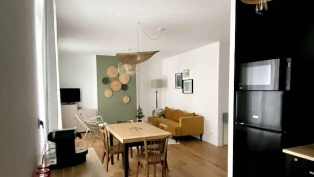 A modern kitchen with a black refrigerator, a dining area with a wooden table and chairs, and a living room with a yellow sofa. - Champagne! Spacious apartment (Reims)