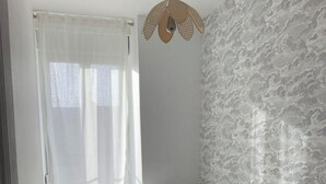 A bedroom with a bed, a window with sheer curtains, a patterned wall, and a hanging light fixture. - Champagne! Spacious apartment (Reims)