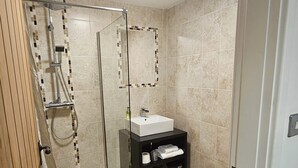Un baño moderno con ducha de vidrio, lavamanos blanco y tocador negro.