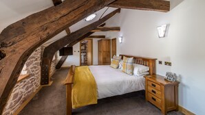 Un dormitorio con techo inclinado, vigas de madera a la vista, una cama con una manta amarilla, mesitas de noche de madera y una pared de piedra.