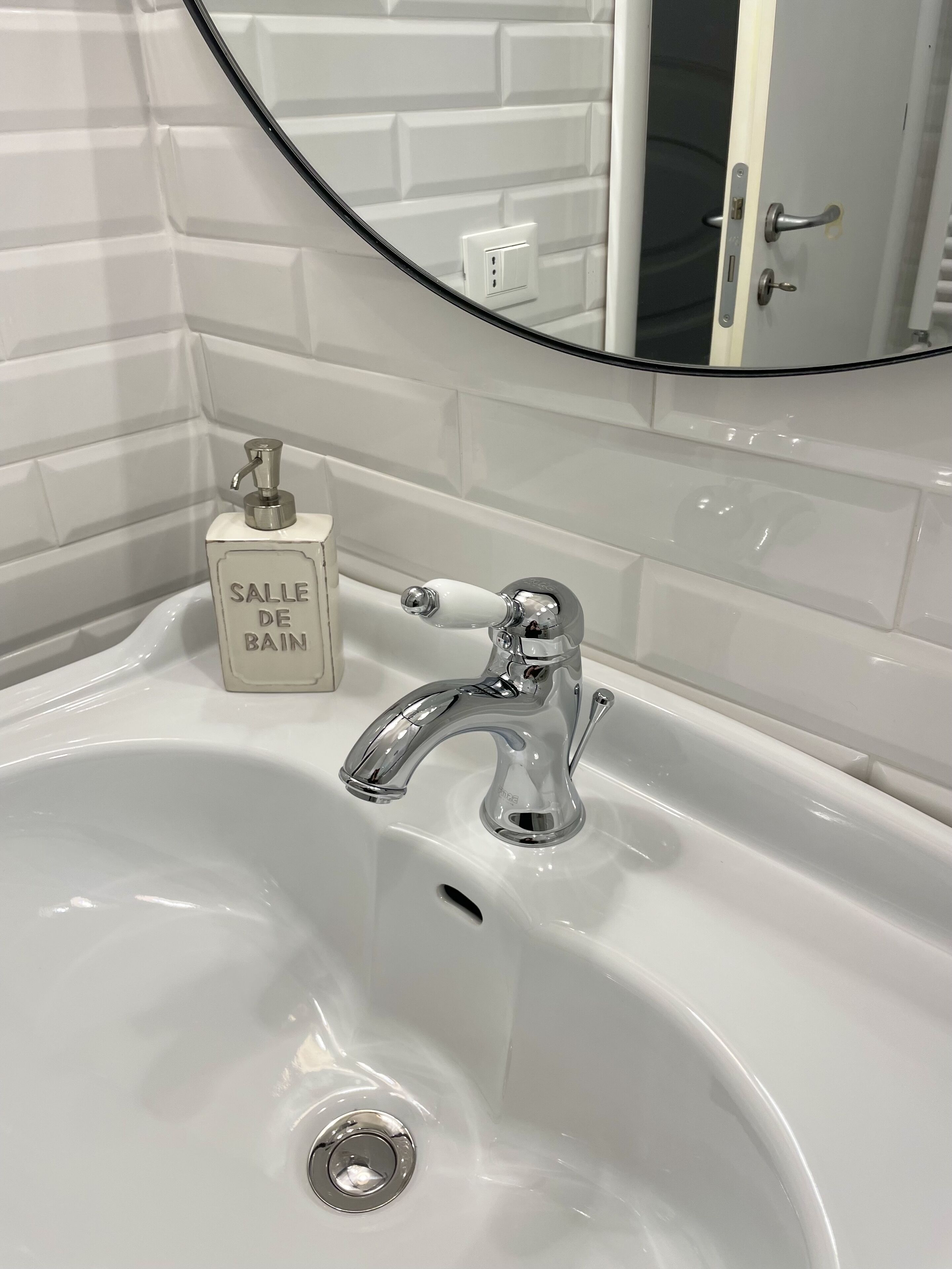 A bathroom with a white sink, a mirror, and a soap dispenser labeled "SALLE DE BAIN".