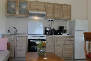A compact kitchen with wooden cabinets, a white refrigerator, a stove, and a coffee maker. - Olive Garden House (Festos)