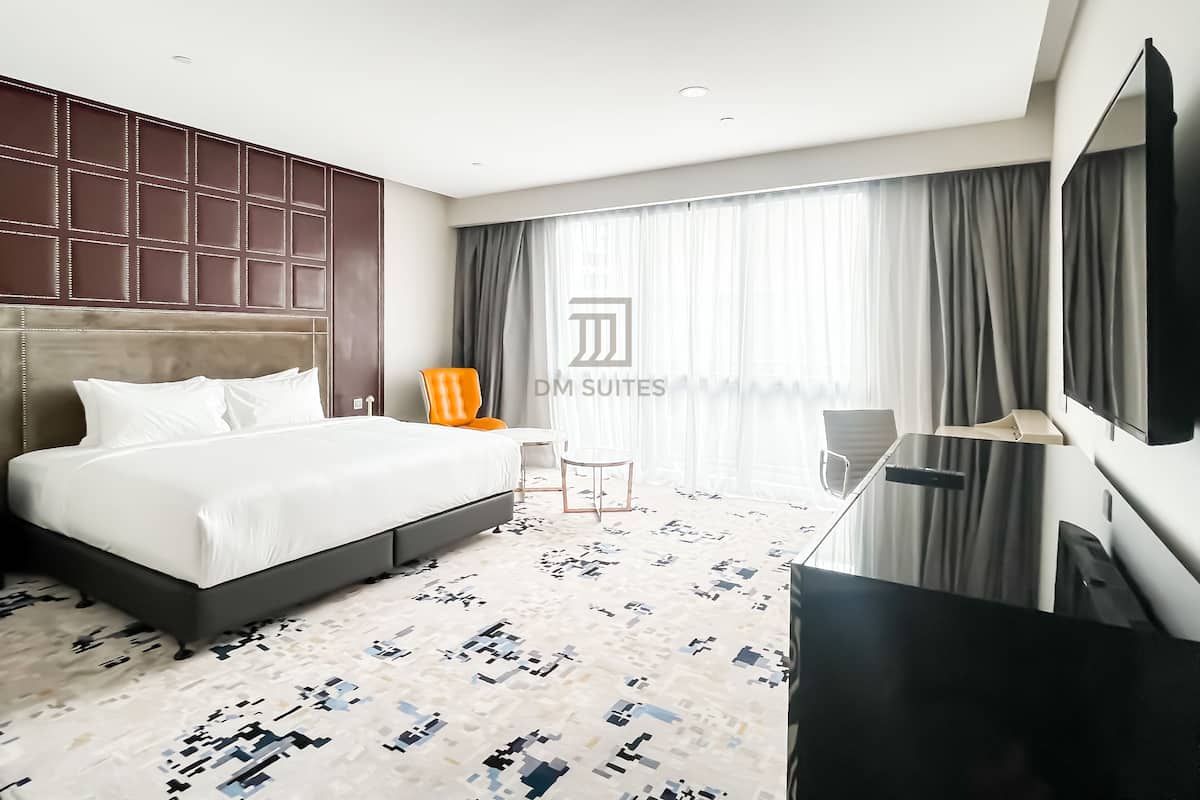 A modern hotel room with a large bed, a flat-screen TV, a desk, and a chair.