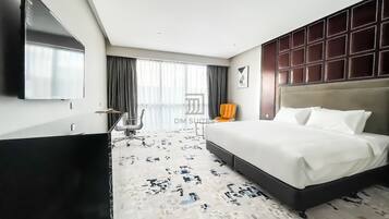A hotel room with a large bed, a flat-screen TV, a desk, and a chair.