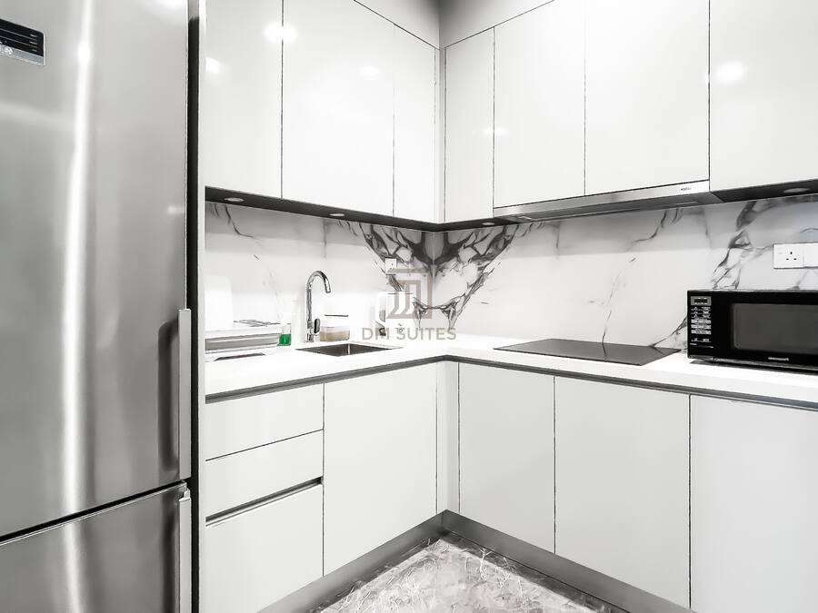 A modern kitchen with white cabinets, a stainless steel refrigerator, a marble backsplash, and a black microwave.
