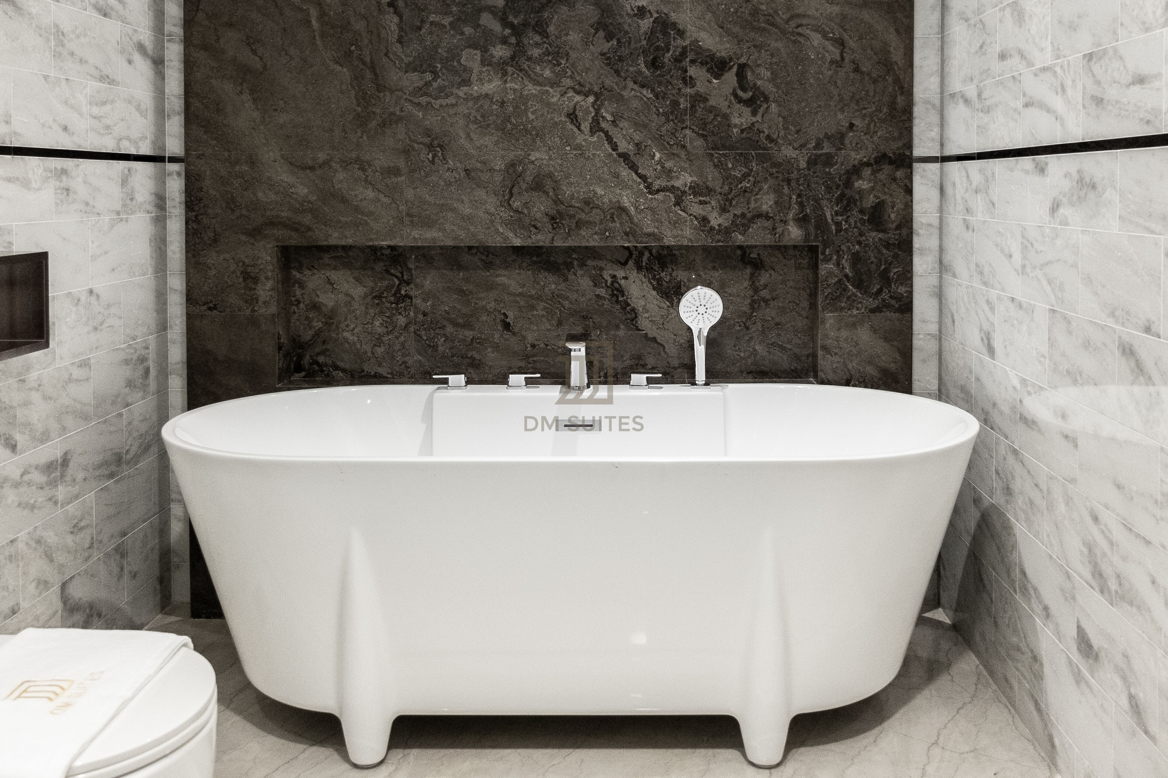 A modern bathroom with a freestanding bathtub, marble walls, and a visible logo on the wall.