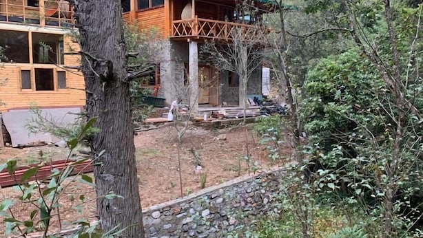A wooden cabin with a green roof, surrounded by dense forest. - Forest View farmhouse stay (Kosiyakutoli)